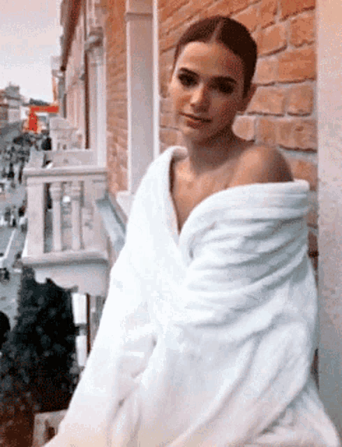 a woman is wrapped in a white robe and standing on a balcony