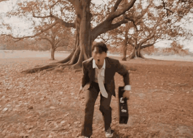 a man in a suit and tie is running in a field holding a skateboard