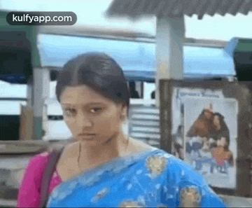 a woman in a blue saree is standing in front of a bus and looking at the camera .