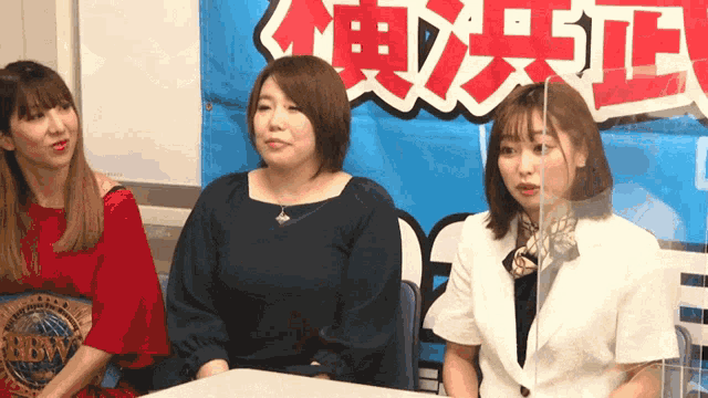 three women sit at a table in front of a sign that says ' tokyo '