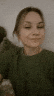 a young woman in a green shirt is sitting on a couch and smiling .