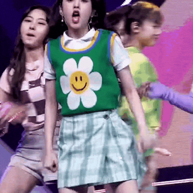 a girl in a green vest with a smiley face on it is dancing on stage .