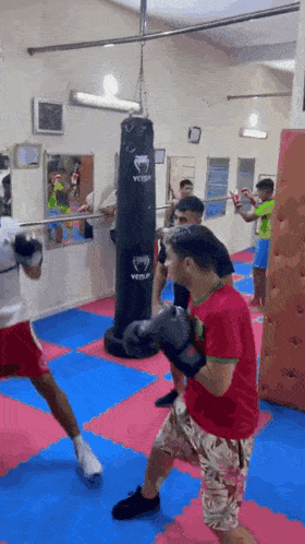 a boy in a red shirt is boxing in a gym with a venum punching bag