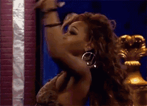 a woman is dancing in front of a brick wall and a gold throne .