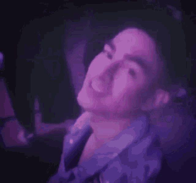 a close up of a man 's face with purple lights behind him .