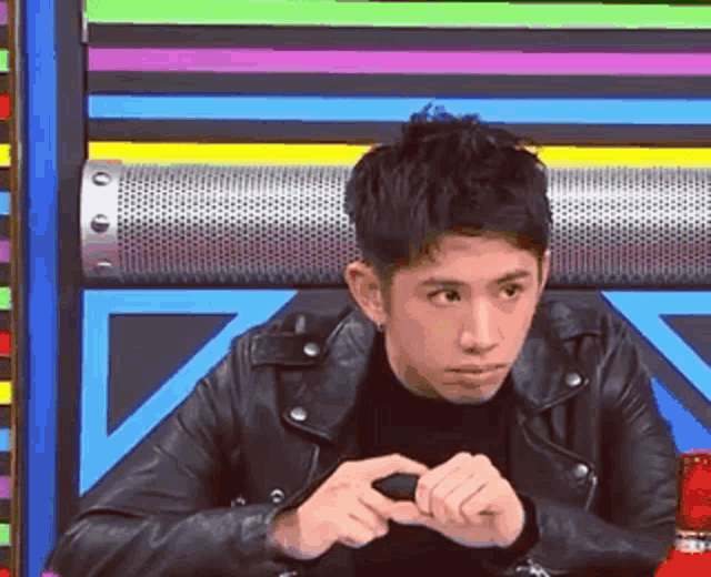 a man in a black leather jacket is sitting in front of a colorful wall .