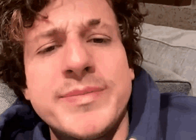 a close up of a man 's face with curly hair and a blue hoodie .
