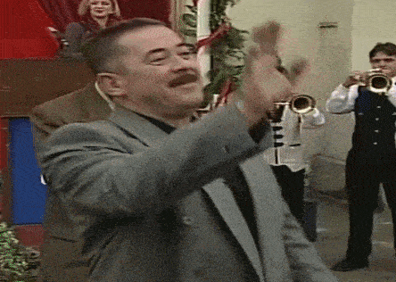 a man in a suit stands in front of a group of men playing trumpets