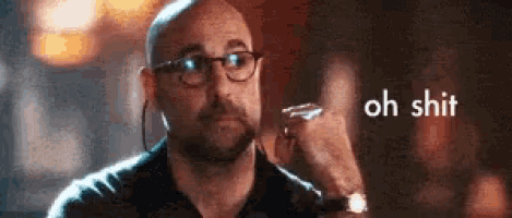 a bald man wearing glasses and ear buds is holding a glass and says oh shit .