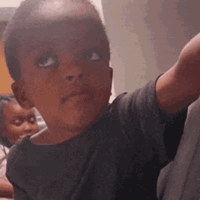 a young boy is making a funny face and looking at the camera while a woman looks on .