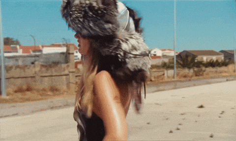 a woman wearing a fur hat and sunglasses walks down a street