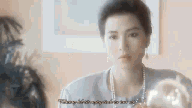 a woman wearing a necklace and earrings is talking to someone in a room .