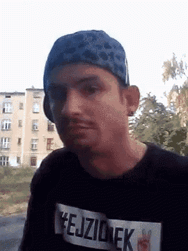 a man wearing a hat and a shirt that says vejzidek looks at the camera