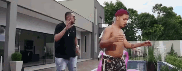 a man without a shirt is standing next to another man in front of a swimming pool .