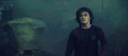 harry potter is holding a glowing object in his hand in a dark room .