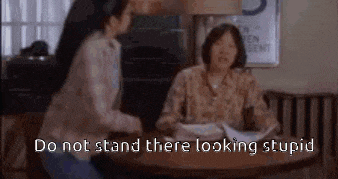 two women are sitting at a table with a sign that says `` do not stand there looking stupid `` .