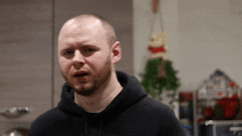 a bald man with a beard wearing a black hoodie looks at the camera