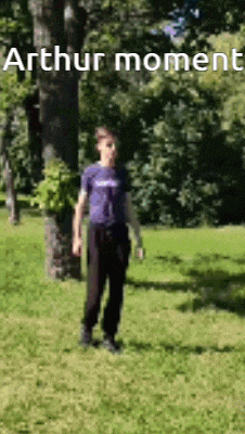 a man in a purple shirt is standing in the grass in a park with trees in the background .