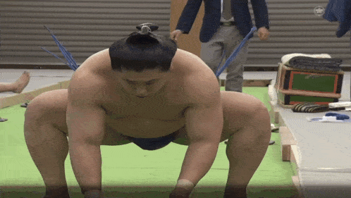 a sumo wrestler is kneeling down on a mat