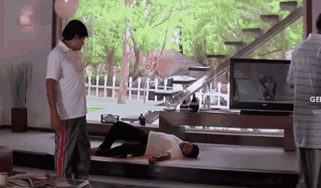 a man is laying on the floor in front of a television while another man stands next to him .