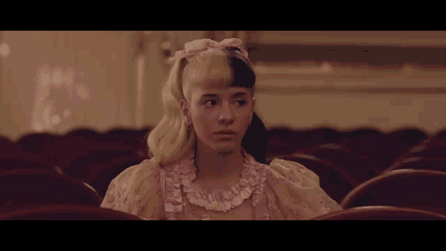 a girl with half blonde and half black hair is sitting in a theatre .