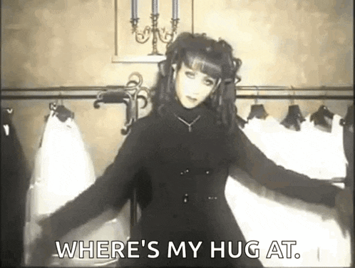 a woman in a black dress is standing in a room with clothes hanging on a rack and a candle .