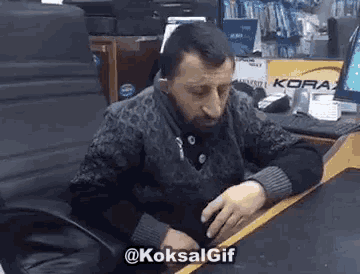 a man with a beard is sitting at a desk in front of a computer and a sign that says kora .