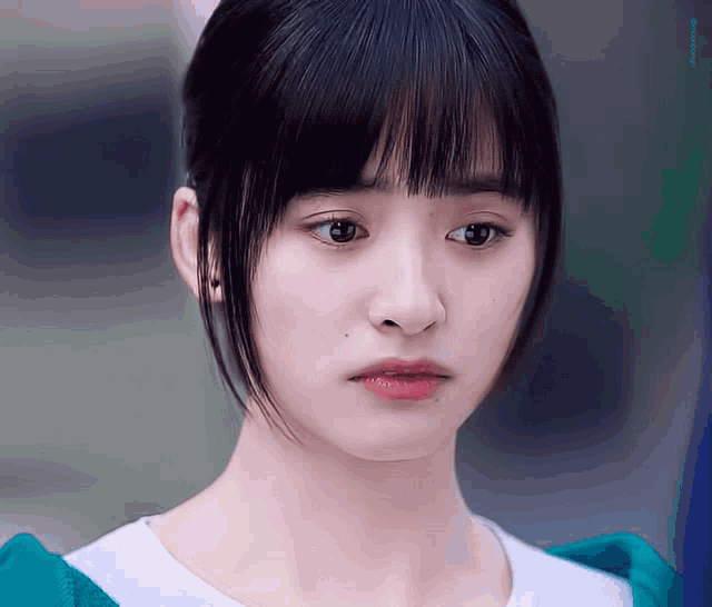a close up of a woman 's face with a white shirt and a green sweater