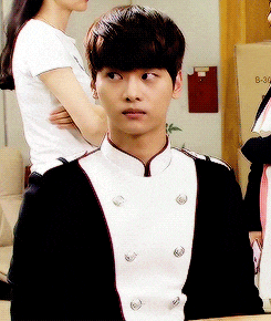 a man in a black and white uniform looks at the camera while a woman stands behind him