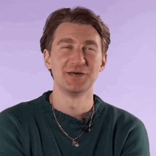 a man wearing a green sweater and a necklace with a pendant that says r on it
