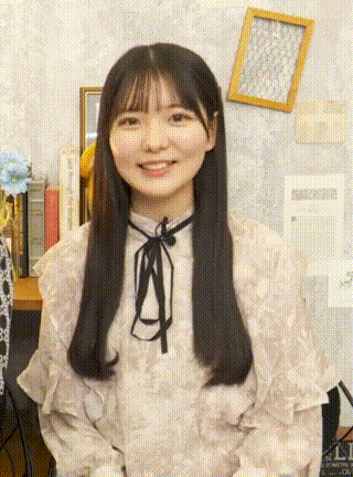 a girl with long black hair is smiling and wearing a white shirt with ruffles and a black bow .