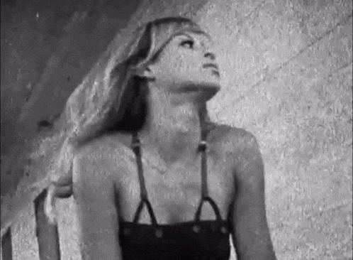 a black and white photo of a woman in a bikini looking up at the sky .