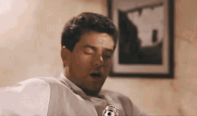 a man in a white shirt is sitting at a table with his eyes closed and his mouth open .