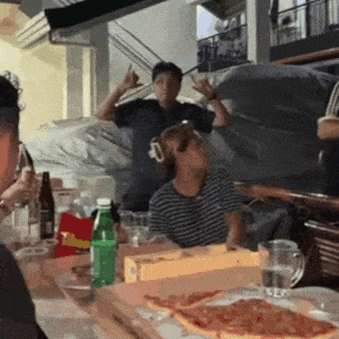 a group of people are sitting around a table with a box of pizza