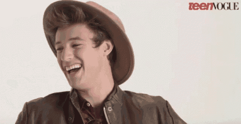 a young man wearing a hat and a leather jacket is laughing in front of a teen vogue logo