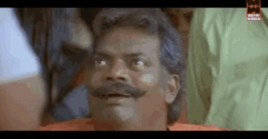 a man with a mustache is making a funny face in front of a crowd of people .