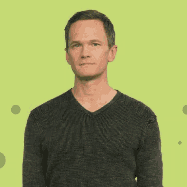 a man in a gray sweater is making a funny face while talking on a green background .