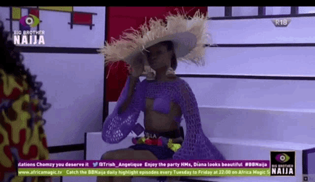 a woman wearing a hat and a purple top is sitting on a couch on a big brother naija show