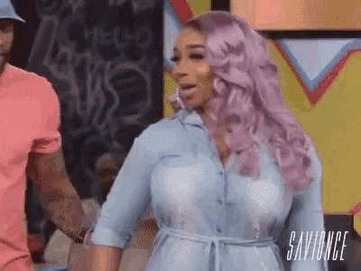 a woman with pink hair is standing next to a man in a pink shirt and holding his hand .