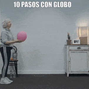 an older woman is throwing a pink balloon in a living room .