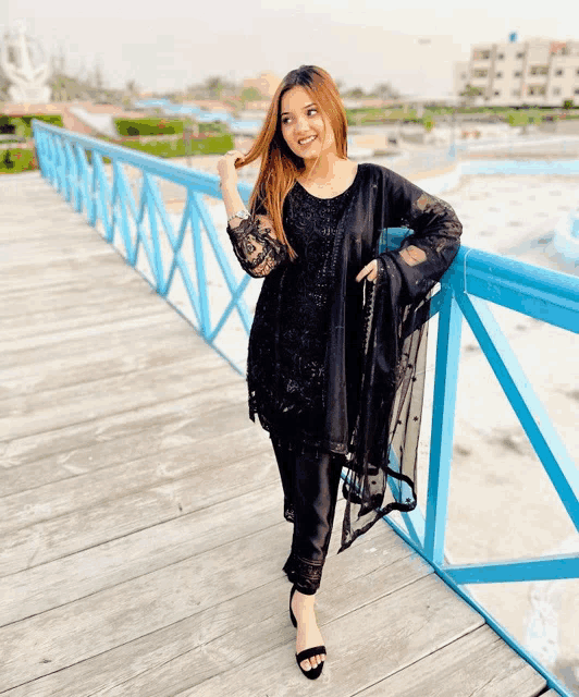 a woman in a black dress is standing on a wooden bridge