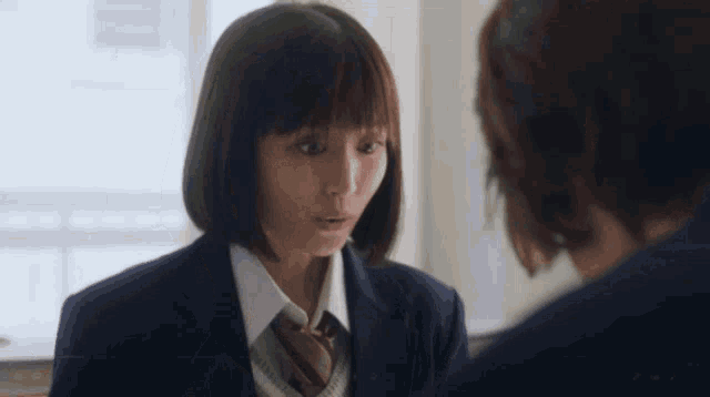 a girl in a school uniform and tie is talking to a boy