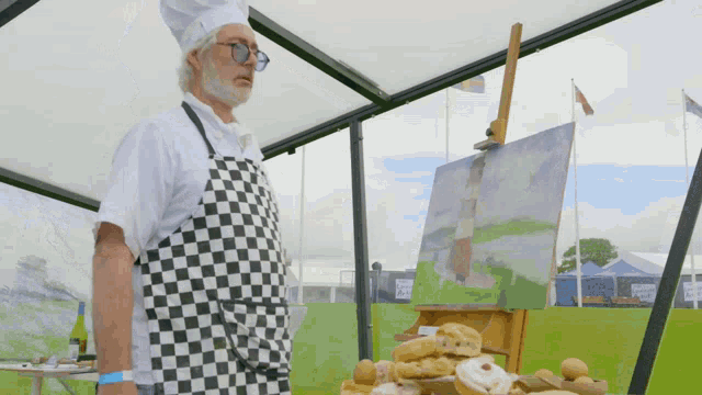 a man in a chef hat and apron stands in front of a painting