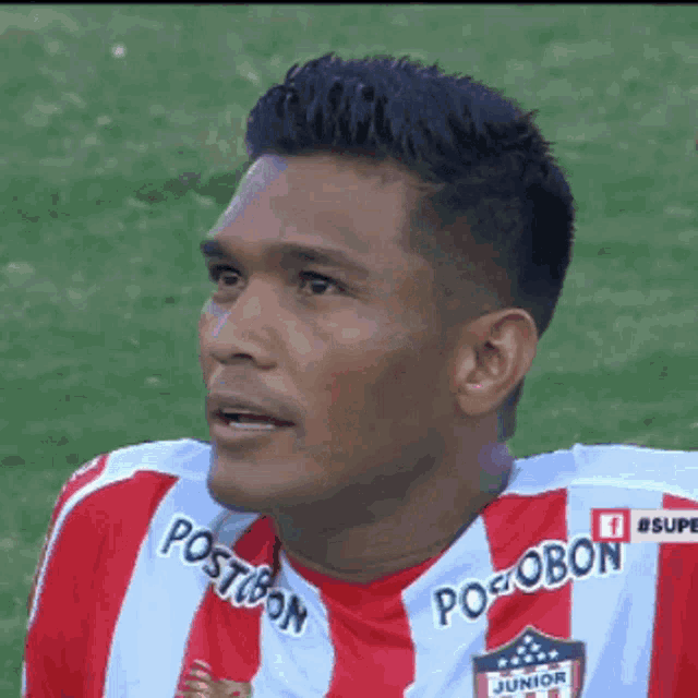 a man wearing a red and white striped jersey that says postobon junior on it