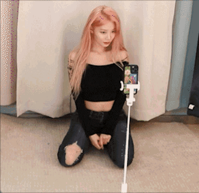 a woman with pink hair is kneeling down and holding a cell phone