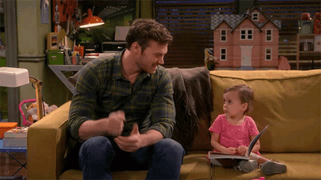 a man and a little girl are sitting on a couch with a doll house in the background ..