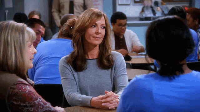 a woman in a grey sweater sits at a table with other people