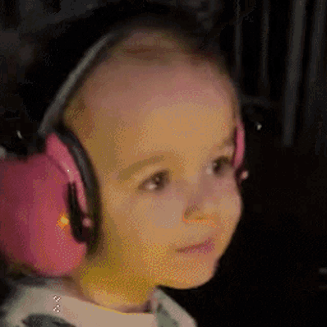 a baby wearing pink ear muffs is looking at the camera