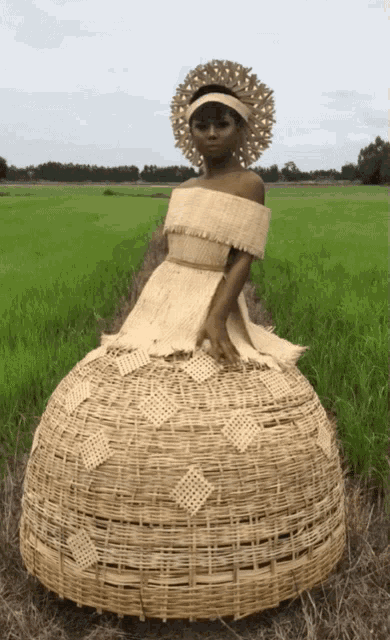 a woman wearing a wicker dress and hat stands in a field