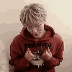 a young man wearing a red thrasher hoodie is sitting on a couch .